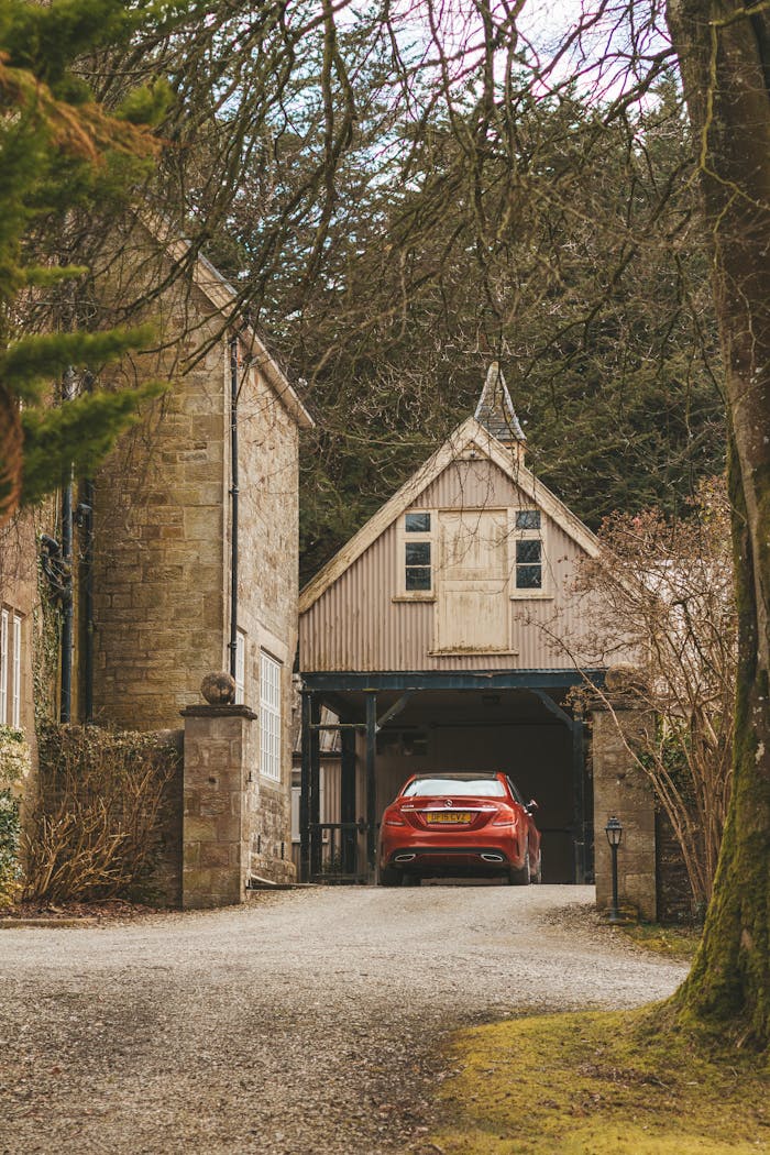A quaint stone house with a red car parked in a garage nestled in the Welsh countryside.