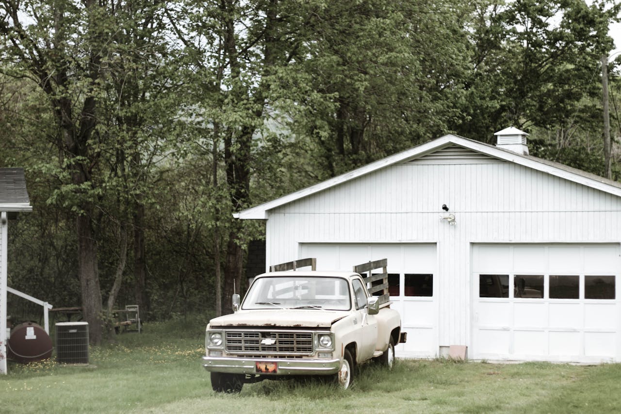 A classic vintage truck parked beside a rustic garage amidst lush greenery in Asheville, NC.